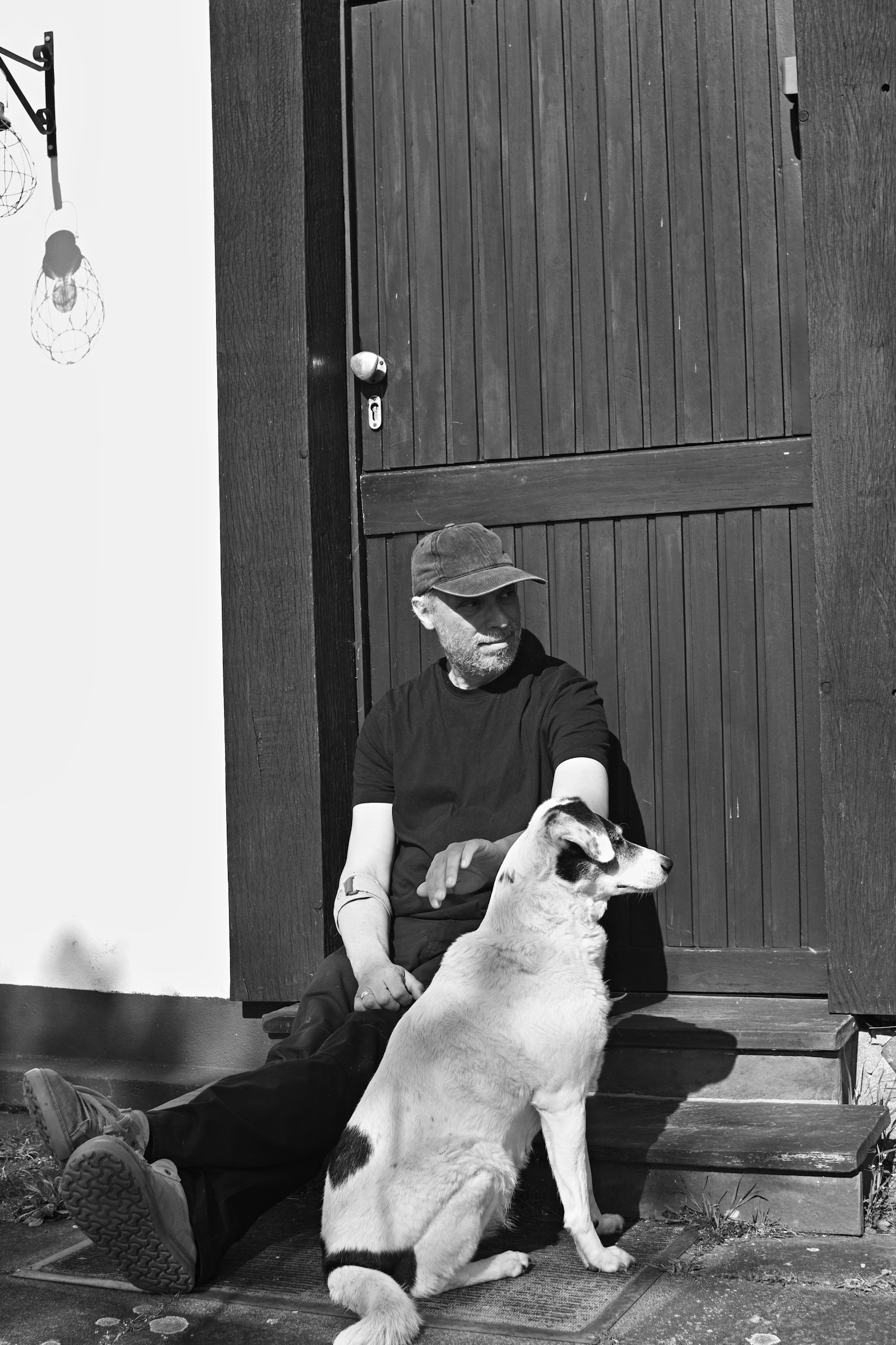 a man and a black and white dog sitting in front of a cottage door