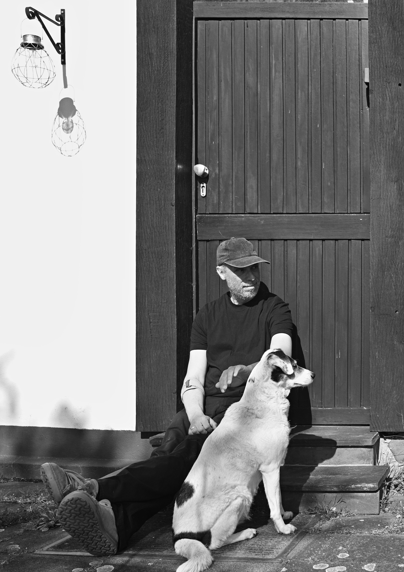 black and white picture of a man and a black and white dog sitting in front of a doorway.