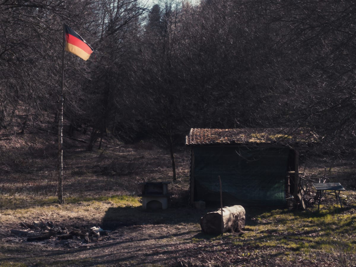 A rundown wooden shed with the national flag of Germany beside it.