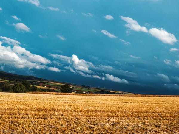 a stormy summer landscape with a harvested field and storm clouds in the valley behind it.