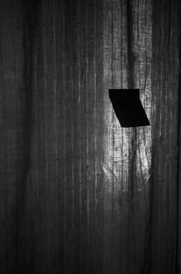 Black and white photograph of a post-it note tucked to a glass door with a curtain behind it.